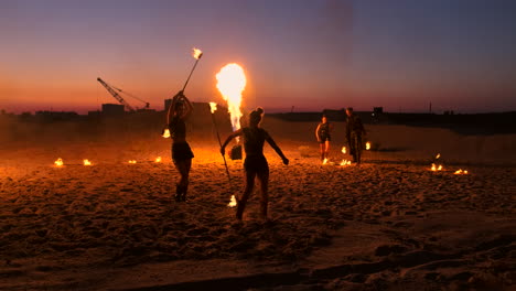 Artistas-Profesionales-Muestran-Un-Espectáculo-De-Fuego-En-Un-Festival-De-Verano-En-La-Arena-A-Cámara-Lenta.-Los-Acróbatas-De-La-Cuarta-Persona-Del-Circo-Trabajan-Con-Fuego-Por-La-Noche-En-La-Playa.